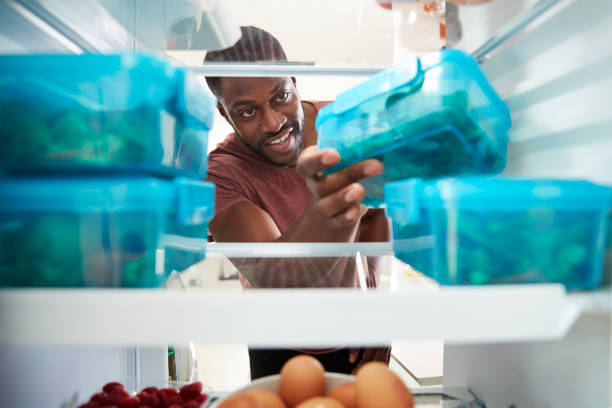 view looking out from inside of refrigerator as man takes out healthy packed lunch in container - staple remover imagens e fotografias de stock