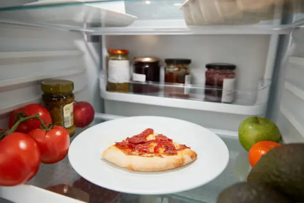 View Inside Refrigerator Of Leftover Takeaway Pizza Slice On Shelf