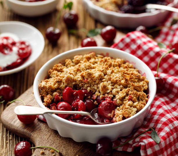 cherry crumble, stewed fruits topped with crumble of oatmeal, almond flour, butter and sugar  in a baking dish on a wooden table - crumble imagens e fotografias de stock