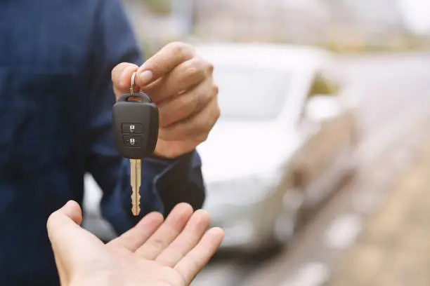 Photo of Car key, businessman handing over gives the car key to the other woman on car background.