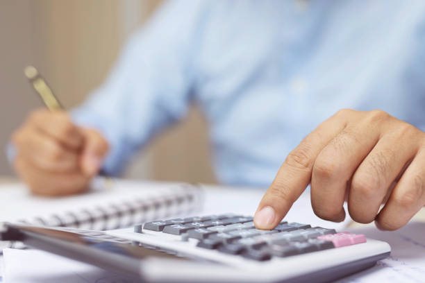 istock Close up business man hand is writing in a notebook and using calculator counting making notes Accounting at doing finance at office. Savings finances concept. note pad. Leave space for writing text. 1163966310