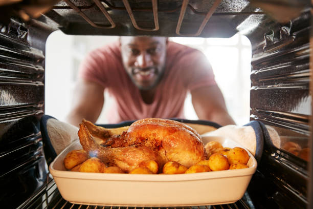 男が日曜日のローストチキンディナーを調理するようにオーブンの中から外を見る - chicken roast ストックフォトと画像