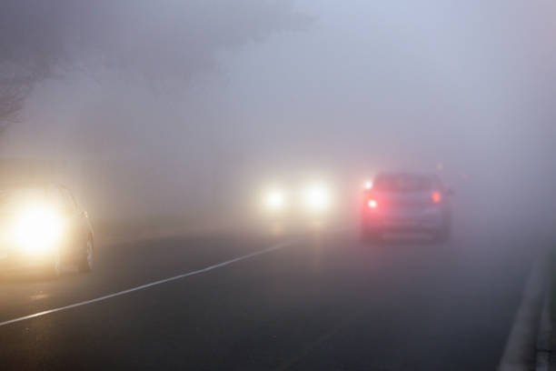 los coches de los viajeros conducen a través de la niebla en la calle de la ciudad en el crepúsculo - niebla fotografías e imágenes de stock