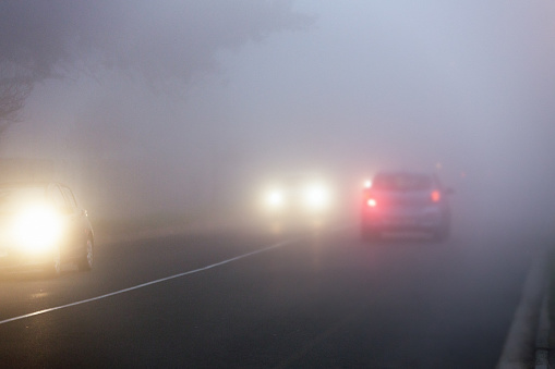 Commuters' cars drive through fog on city street at twilight