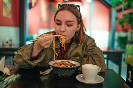 Teenage girl eating Asian noodle in a restaurant