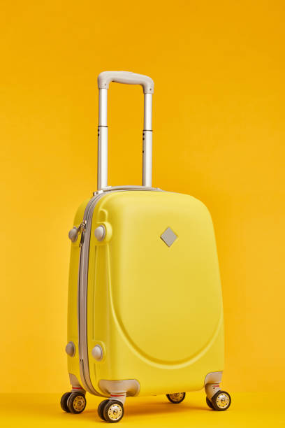 istock yellow travel bag with handle on wheels isolated on orange 1163977925