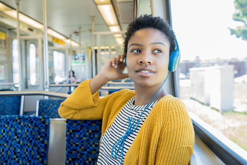Beautiful African American young woman listens to music with headphones while riding commuter train in the city