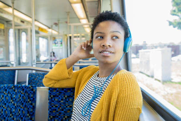 Beautiful African American young woman listens to music with headphones while riding commuter train in the city Beautiful African American young woman listens to music with headphones while riding commuter train in the city vehicle interior audio stock pictures, royalty-free photos & images