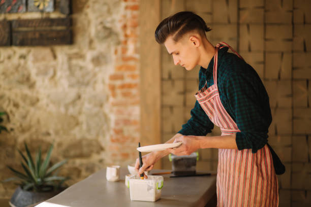 istock Potter making ornament on ceramic plate. Professional male potter draw a pencil on ceramic product 1163985255