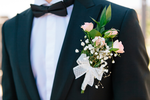 Closeup pink roses boutonniere with the decor on a grooms dark blue elegant jacket, selective focus