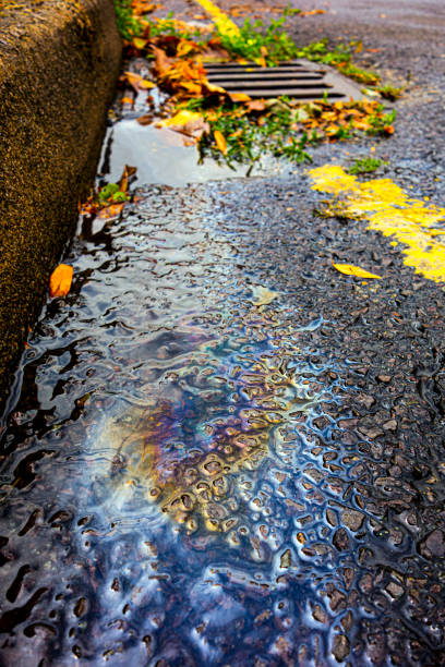 Spilt Petrol Gasoline Oil Running Down a Drain On a Road Gutter Environmental Pollution
