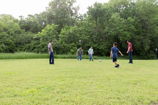 Male family members play soccer together in a field during a family reunion.