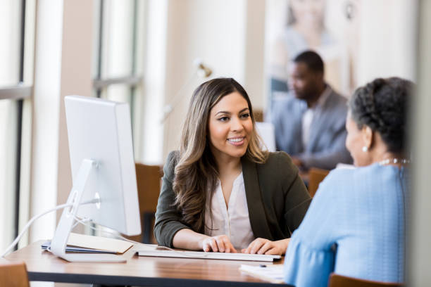 Bank manager smiles at customer as she types in information As she types in the information needed to open a new account, the bank manager smiles at the mature adult customer. types of loans stock pictures, royalty-free photos & images