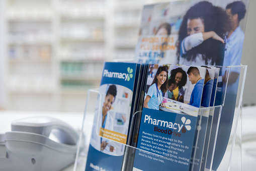 Informational brochures and flyers sit on a pharmacy counter. The brochures and flyers detail the pharmacy's services.