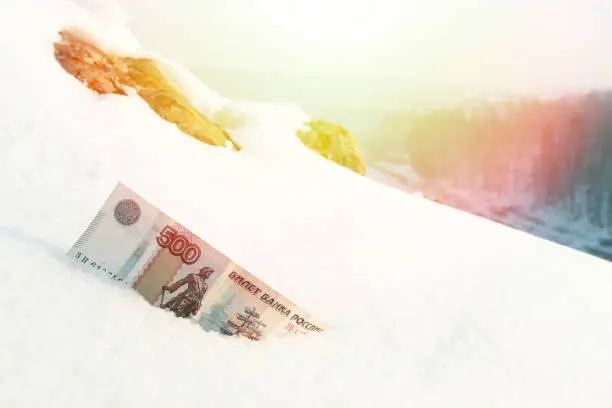 banknote worth 500 rubles in the snow, sunlight and forest in the distance