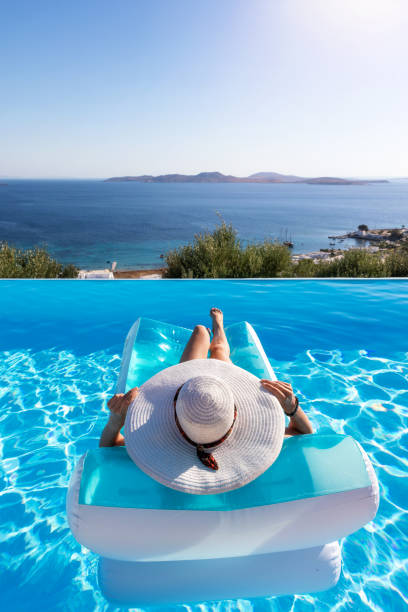 женщина плавает в бассейне и наслаждается видом на море - luxury vacations swimming pool lifestyles стоковые фото и изображения