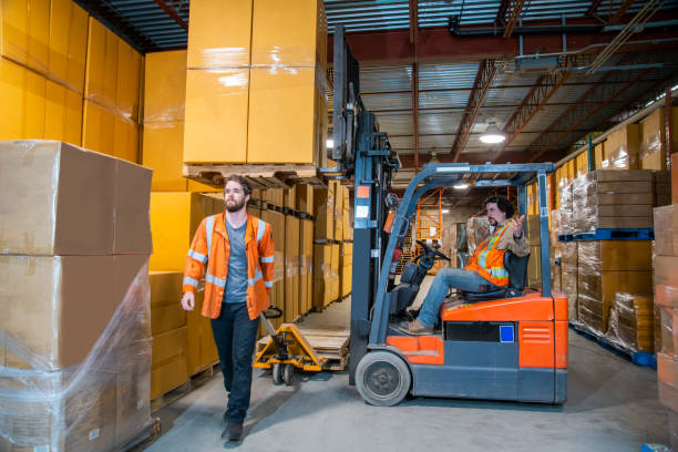 istock An industrial warehouse workplace safety topic.  A worker in the danger zone, walking under a raised forklift carrying a load. 1164009645