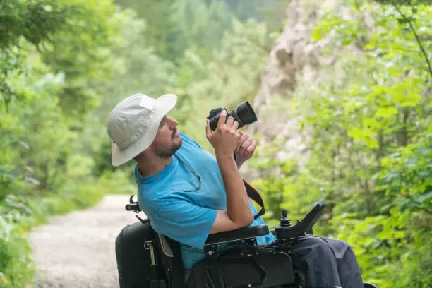 Photo of man on electric wheelchair using mirrorless camera nature, enjoying freedom and doing art