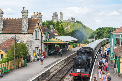 Corfe Castle, United Kingdom - July 8th, 2017 :  A restored steam train arriving at the railway station in the village of Corfe Castle in Dorset, UK.  The restored steam train operates daily between the towns of Swanage and Wareham in Dorset, UK. Passengers can be seen waiting to board the train.