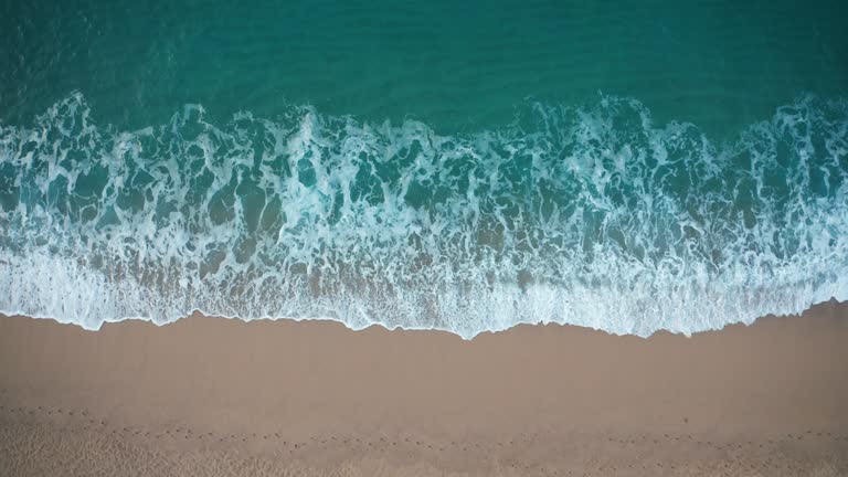 Top view of blue waves crashing against sand beach