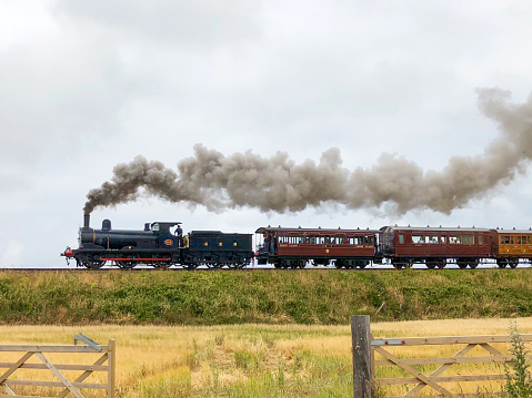 Sheringham, Norfolk, United Kingdom - July 11th, 2018 :  A steam train belonging to the North Norfolk Railway travelling between the two coastal towns of Sheringham and Holt in North Norfolk.  This particular section of track has a steady incline which nescessitates a bit more power being applied, hence the increase in smoke from the steam engine.