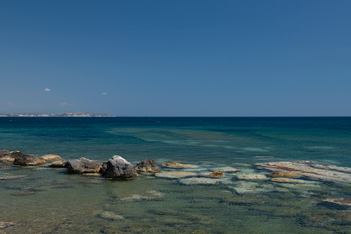 The view of a rocky shore or beach with orange and red rocky ground, boulder, pebbles and sand on the Greek Island of Chios in the Aegean Sea on a sunny afternoon in summer. Many refugees travelling from Turkey to Greece have landed on this particular beach (Agia Ermioni). The image was captured with a full frame DSLR camera with a fast lens at low ISO resulting in a clean large file.