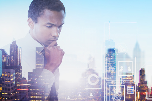 Pensive African American businessman standing over blurred cityscape background with double exposure of business interface. Concept of hi tech startup. Toned image