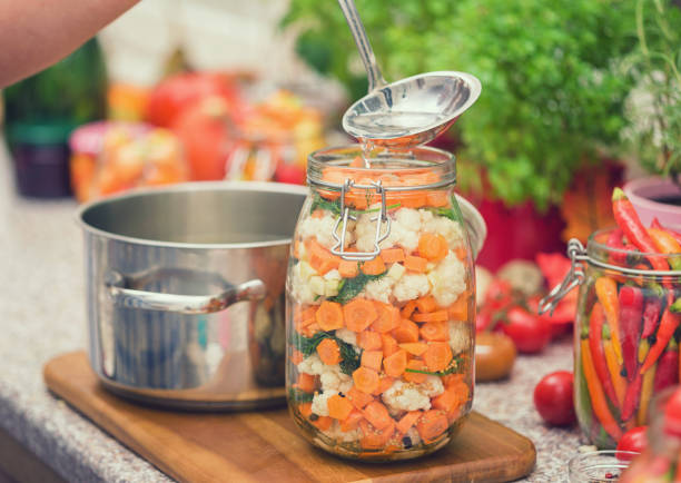 Young women preserving fresh organic cauliflower,carrots and garlic in a jars at home
