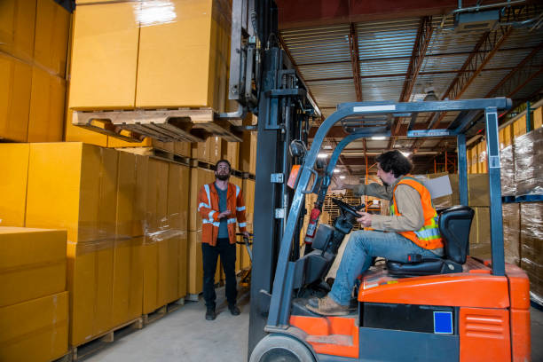 istock An industrial warehouse workplace safety topic.  A worker in the danger zone, walking under a raised forklift carrying a load. 1164017636