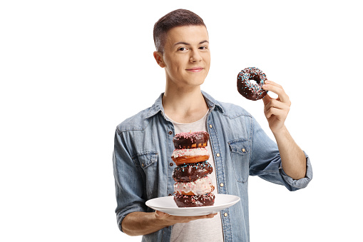 Male teenager holding a plate with a pile of chocolate donuts isolated on white background