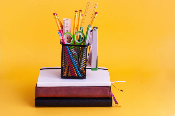 istock Bright modern minimalistic stationery for schoolwork in a glass for stationery on a stack of notebooks on a yellow background. Back to school concept 1164022747