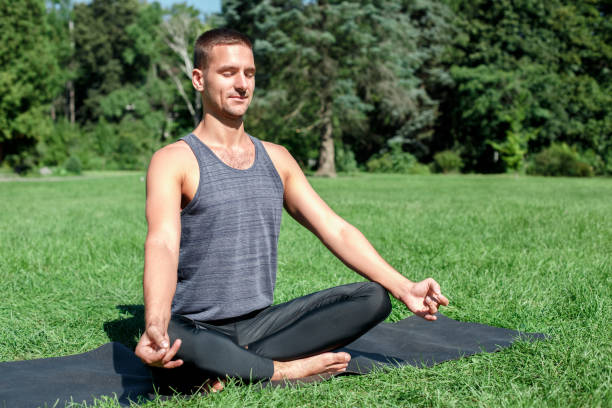 istock Healthy Lifestyle. Man practicing yoga outdoors sitting in lotus pose doing meditation happy side view 1164033421