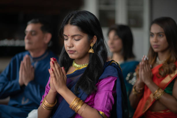 une belle famille indienne s'assied dans leur salon un après-midi priant ensemble. ils célèbrent et remercient pendant les vacances diwali. ils se lient comme ils sont enfilés dans des vêtements traditionnels. - hinduism photos et images de collection