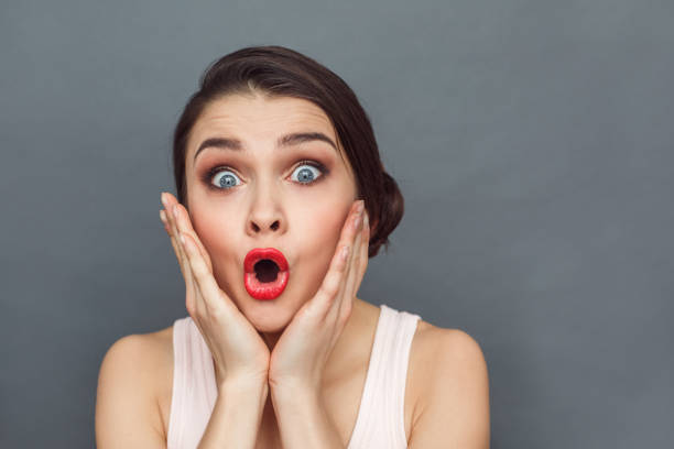 istock Freestyle. Woman standing isolated on grey holding face looking camera impressed close-up 1164033538