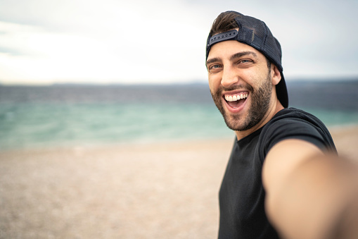 Portrait of happy young man taking a selfie at the beach