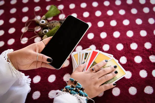 Photo of Fortune teller reading fortune lines on screen smartphone modern horoscopes online fortune telling application Palmistry Psychic readings and clairvoyance hands with Tarot cards divination