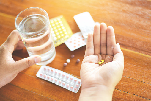 Contraceptive pill prevent pregnancy contraception concept / Woman holding pill and glass of water in hands taking emergency medicine birth control  - health care and medicine