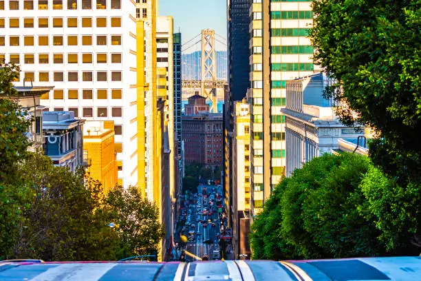 City street view in San Francisco, California uphill looking down between buildings and other architecture at Oakland Bay Bridge over the ocean. Unique American city on the west coast of United States