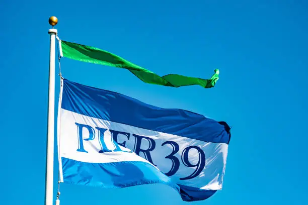 Pier 39 blue, white, green flag on pole at Fishermans Wharf in San Francisco, California, west coast United States. Famous location and popular tourist attraction.