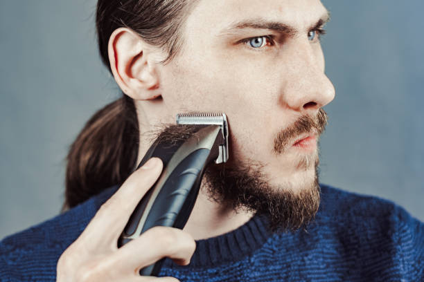 istock guy shaves his beard with an electric razor 1164056858