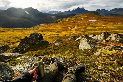 Man holding a cup of coffee with golden landscapes in the background on Lofoten Islands