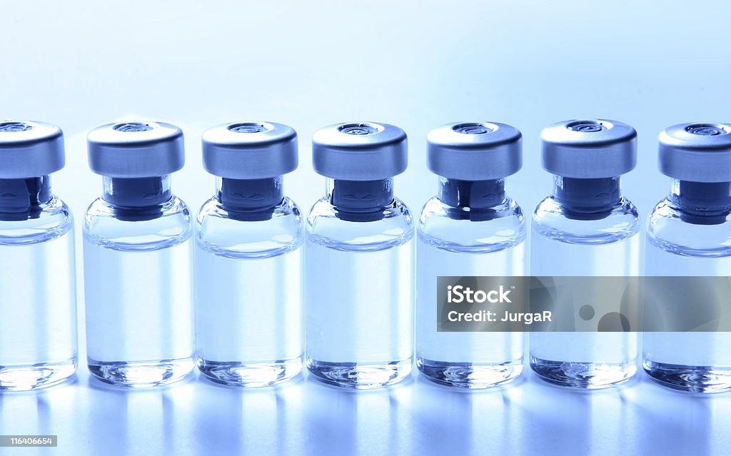 Medical Series - Vials with Medication in a row Close-up of a series of many small generic medical vials standing in a row filled with liquid medication. No labels on the seven bottles. Concepts like vaccination, flu shot. Image is blue tinted. Studio shot. Vial Stock Photo