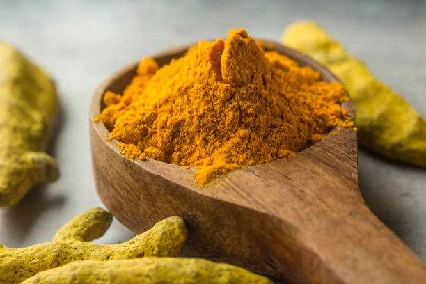 Turmeric roots and powder in wood spoon stock photo