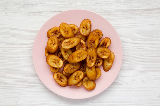 Homemade fried plantains on a pink plate over white wooden background, top view. Flat lay, overhead, from above. Close-up. Homemade fried plantains on a pink plate over white wooden background, top view. Flat lay, overhead, from above. Close-up. plantain stock pictures, royalty-free photos & images