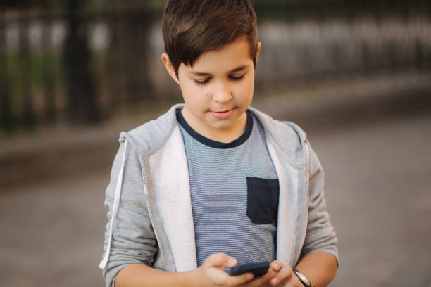 istock Young boy playing with smaptphone. Schoolboy using mobile phone on the street 1164075314