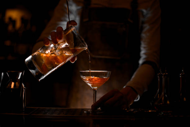Male bartender in leather apron pouring the alcohol cocktail with steel strainer