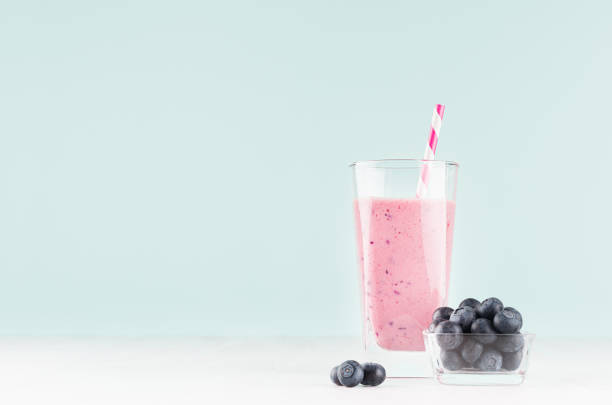 leichte fröhliche frühling milchgetränk mit gestreiftem stroh, heidelbeere in schale auf modernen pastell mint grüne farbe hintergrund und weißen holztisch, kopierraum. - blueberry smoothie glass striped stock-fotos und bilder