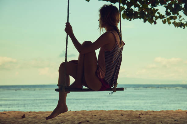 Young woman swinging on a sandy tropical beach.