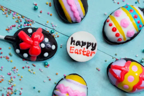 Top view of happy Easter text with colorful chocolate candies on the wooden table