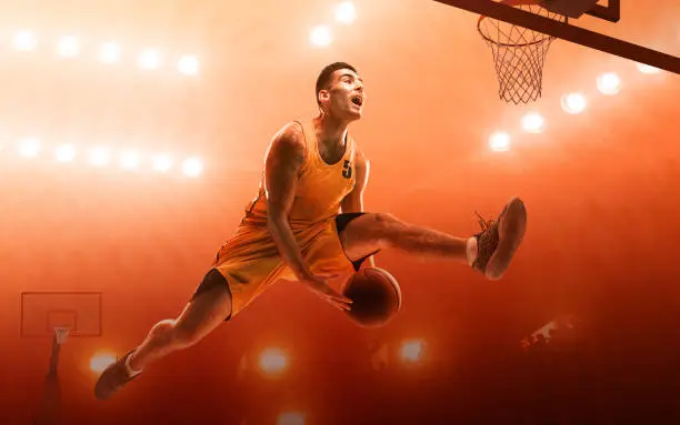 Young muscular basketball player with a ball on floodlight professional court scoring a goal